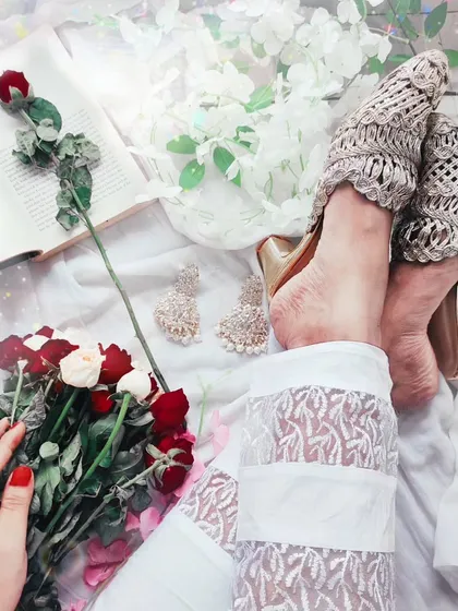 A creative flatlay composition featuring lace pants, heels, roses, and a book. This type of lifestyle photography is great for blogs, social media content, and telling a visual story.