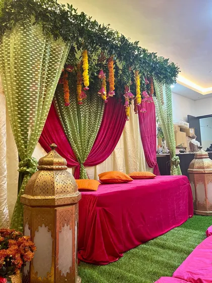 A colorful and cozy Mehendi setup at home. We used bright pink and green drapes, low seating with orange cushions, and traditional lanterns to create a festive vibe.