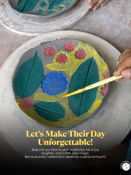 A close-up shot of a child's hands carefully painting a handmade plate with intricate leaf designs during a birthday workshop.