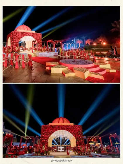 The Royal Rajputana mandap illuminated at night with dramatic spotlights, showcasing how lighting transforms the floral structure into a beacon of celebration against the dark sky.