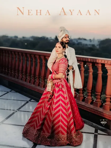 A royal portrait of the couple on a balcony at sunset, showcasing their traditional wedding attire against a beautiful architectural backdrop.