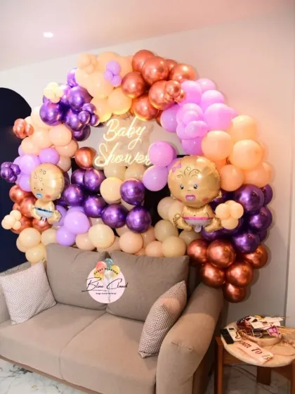 A chic baby shower setup with an organic balloon garland in purple, peach, and chrome tones, complete with a neon sign.