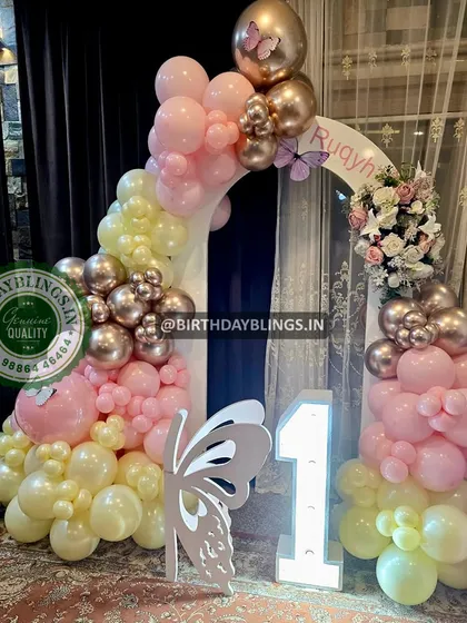 An enchanting butterfly-themed first birthday. The balloon arch in pastel yellow and pink is accented with metallic rose gold, and a large butterfly cutout adds a magical touch.