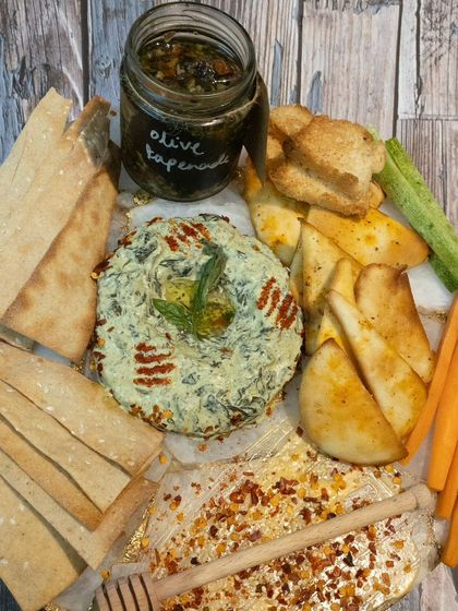 A beautiful cheese and dip platter featuring a spinach-layered cheese ball, olive tapenade, and various crackers and vegetable sticks.