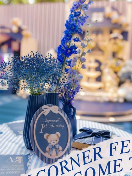 A detailed shot of the table setting, featuring a personalized birthday sign and deep blue floral arrangements that complement the teddy bear theme.
