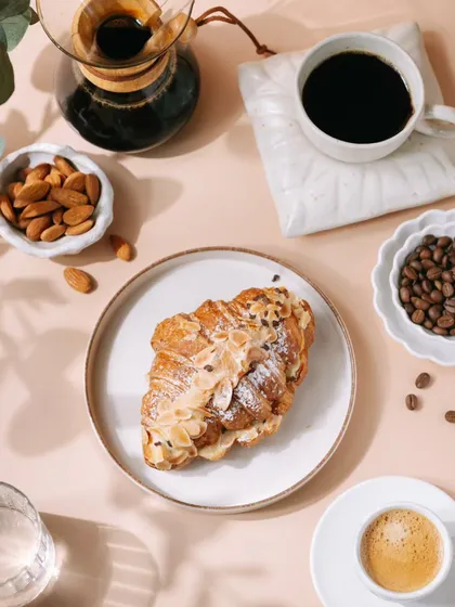 A wider, flatlay view of the almond croissant and coffee setup. This type of shot is great for website banners or magazine features, showing the product in a full, styled scene.