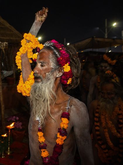 A Naga sadhu with his arm raised, a gesture of blessing and spiritual power, during the Kumbh Mela. The garlands of marigolds add a touch of vibrant color.