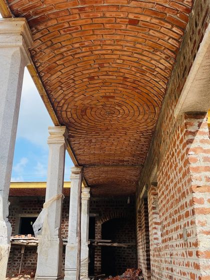A long barrel vault made of brick covers a veranda space. This traditional roofing technique provides a durable and beautiful ceiling, supported by stone pillars for a timeless look.