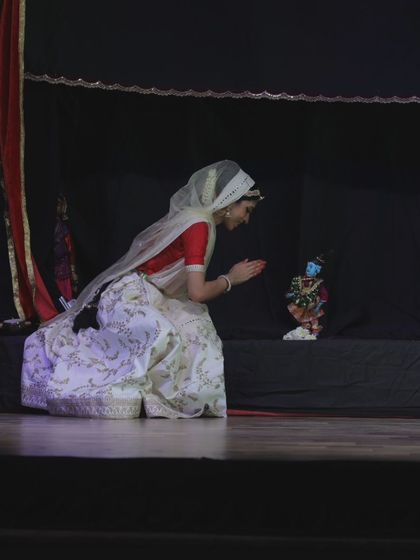 A dancer kneels in devotion before the puppet of Lord Krishna. This fusion of live performance and puppetry is a hallmark of our productions, creating a deeply moving experience.