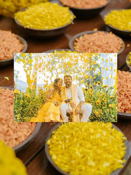 A creative flat-lay style shot of the couple's Haldi portrait surrounded by bowls of flower petals.