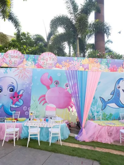 A colorful dining area for an outdoor Under the Sea party, with vibrant backdrops featuring cute sea creatures like octopuses, crabs, and sharks.