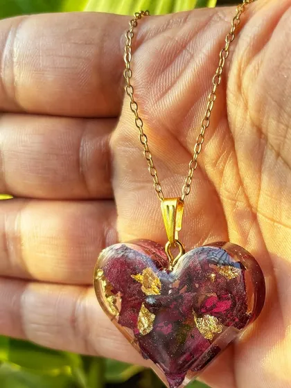 A closer look at the heart-shaped rose petal pendant, showing the delicate gold flakes mixed in with the petals. The gold chain complements the piece beautifully.