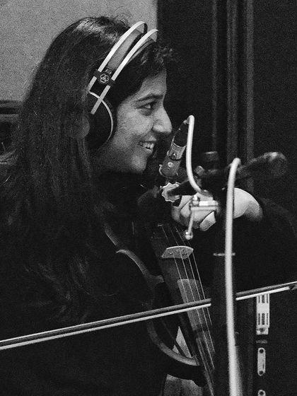 A smiling Apoorva Krishna on violin during a studio session. The joy of creating music is evident even in these behind-the-scenes moments.