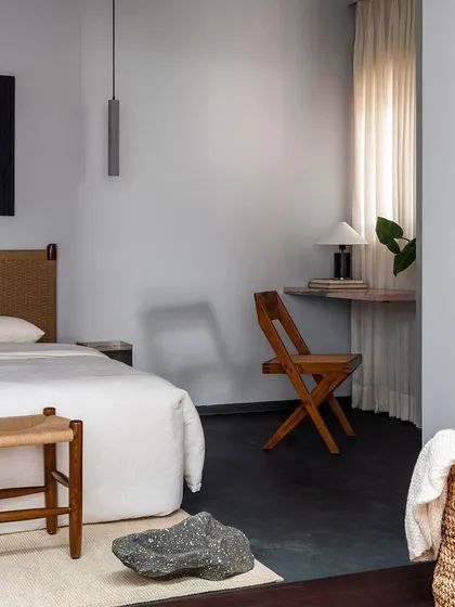 A woven bench sits at the foot of the bed, paired with a wooden folding chair that serves a small desk. I design versatile pieces that can adapt to different needs, ensuring every part of a room is useful.