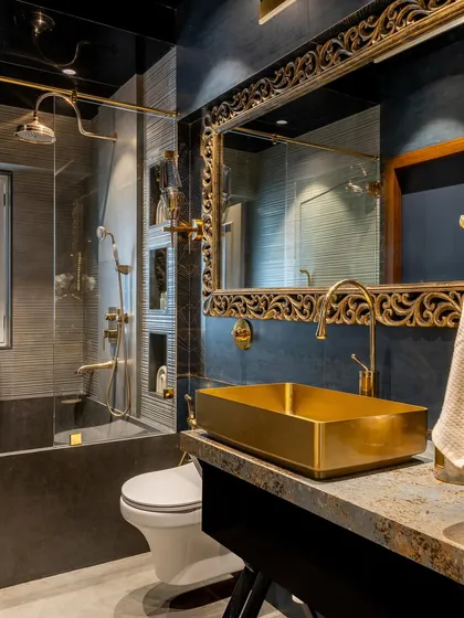 A truly luxurious bathroom experience. This space features dark, textured walls, opulent gold fixtures, a gold-leaf mirror, and a statement golden sink, creating a dramatic and sophisticated ambiance.