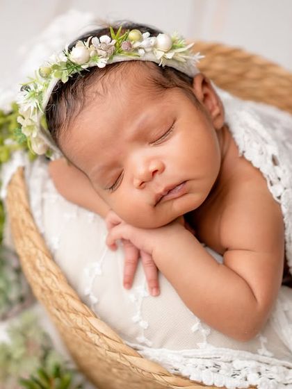 A classic newborn portrait in a basket, wrapped in lace and surrounded by greenery.
