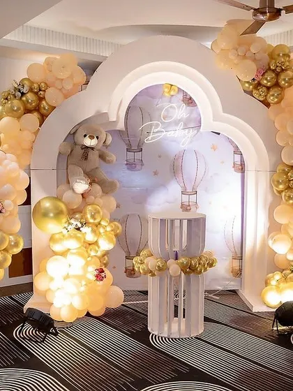 An elegant teddy bear theme for a second birthday, using a palette of champagne, gold, and white. The setup features balloon arches framing a custom backdrop with hot air balloon illustrations.