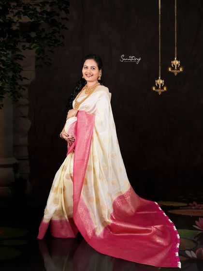 A joyful portrait of a mother-to-be in a classic white and pink saree. The dark background with hanging lamps creates a beautiful contrast, highlighting her radiant smile.