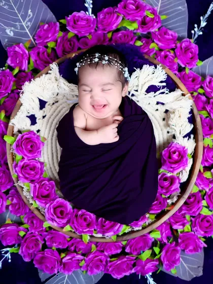 A joyful shot of the newborn smiling and stretching in her sleep, surrounded by purple flowers. These candid moments are truly special.