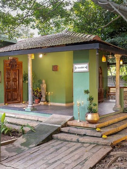 The exterior of the Arundati suite, a charming green cottage with a traditional porch and wooden pillars.