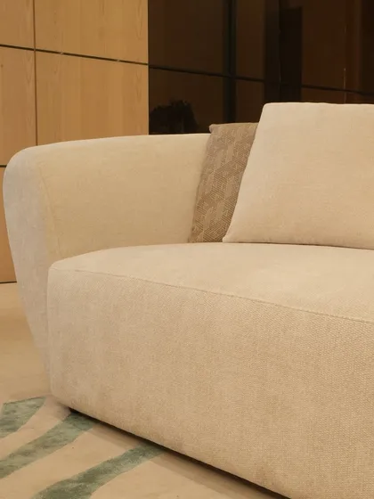 A close-up of the clean lines and gentle curves of one of our custom sofas. Upholstered in a soft, off-white fabric with a contrasting textured cushion, this piece highlights our focus on subtle details and high-quality finishes for modern living.