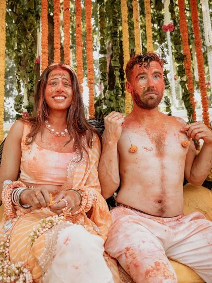 A funny and real moment from a Haldi ceremony. The couple, covered in turmeric paste, share a candid moment, showcasing the lighthearted fun of the event.