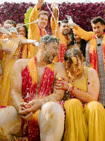 The couple gets drenched with water and blessings by their friends and family. This high-energy shot captures the fun and madness of a Haldi celebration.