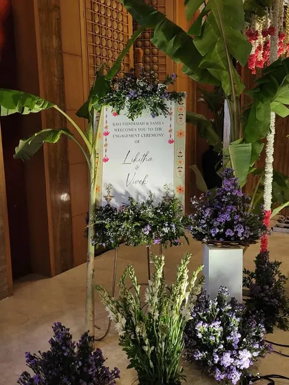 A floral welcome sign for an engagement ceremony, combining traditional motifs with elegant typography and fresh flower arrangements.