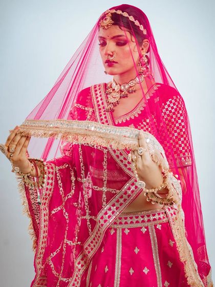 The classic bridal pose with the veil. The sheer pink dupatta adds a layer of mystery and elegance.