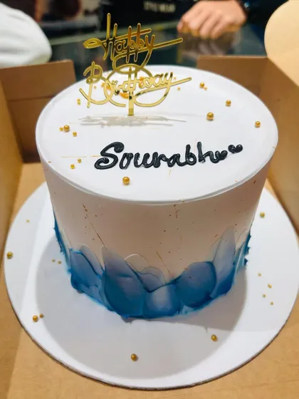 A simple yet elegant birthday cake with a blue watercolor effect and a gold acrylic topper.