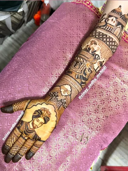The groom's portrait is the centerpiece of this intricate bridal design, complete with a baraat scene featuring elephants and traditional architectural elements on the arm.