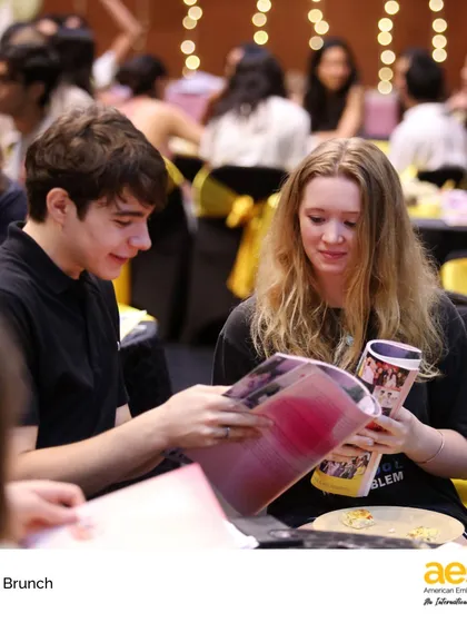 Two seniors look through their yearbooks at the Senior Brunch, reminiscing about their time at the school. It's a moment of reflection and friendship before they embark on their next chapter.