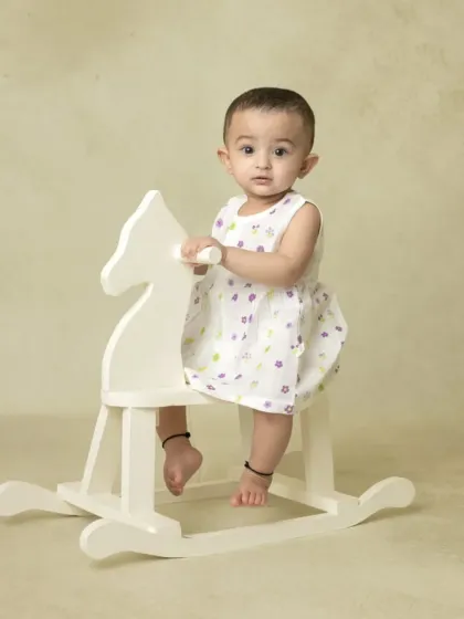 A simple portrait of a baby girl on a white rocking horse against a plain background, capturing a moment of quiet play.