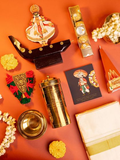 A deconstructed view of the 'Kasavu & Katha' hamper, highlighting each traditional element like the kasavu cloth, brassware, and handcrafted decor against a vibrant orange background.