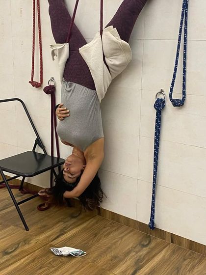 A student in a hanging inversion using the wall ropes. This pose, known as a rope Sirsasana variation, creates space between the vertebrae and is deeply relaxing.