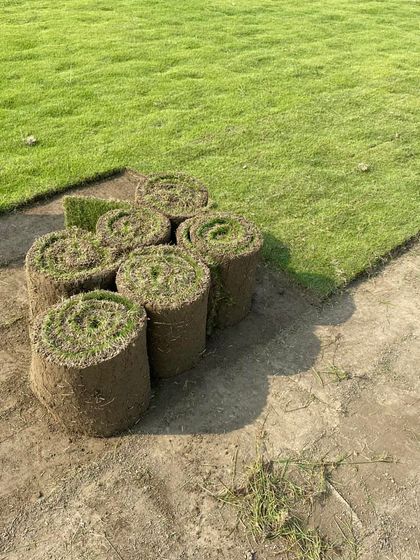 A close-up of the grass rolls, stacked and ready. You can see the rich soil and dense root system that guarantees a healthy lawn.