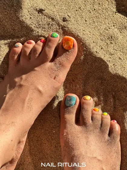 Sun, sand, and the cutest beach-ready toes. This image shows off a vibrant summer pedicure with a different artistic design on each toenail.