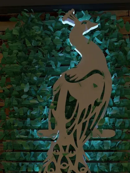 A close-up of the backlit peacock mural from our terrace project. This custom-cut metal art piece is layered over a green wall and illuminated from behind for a dramatic effect at night.