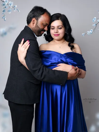 An intimate embrace that showcases the couple's bond. The soft lighting and the rich color of the gown create a warm and romantic atmosphere for this studio maternity portrait.
