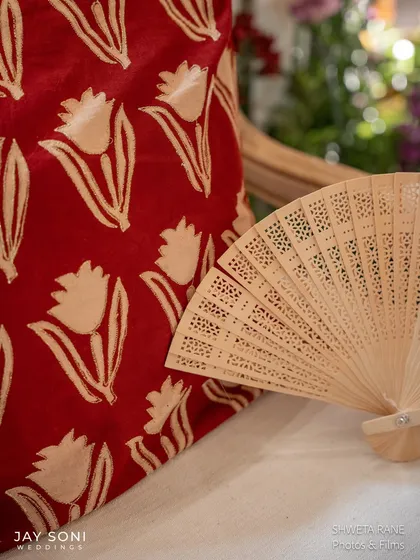 A close-up showing the thoughtful pairing of textures and patterns, with a red block-print cushion and a traditional carved wooden fan.