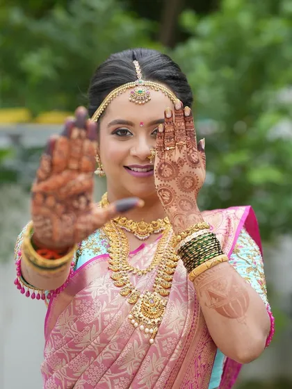 A playful and happy bride showing off her intricate henna. Her hair is styled in a traditional updo, a classic choice that keeps the focus on her radiant face.
