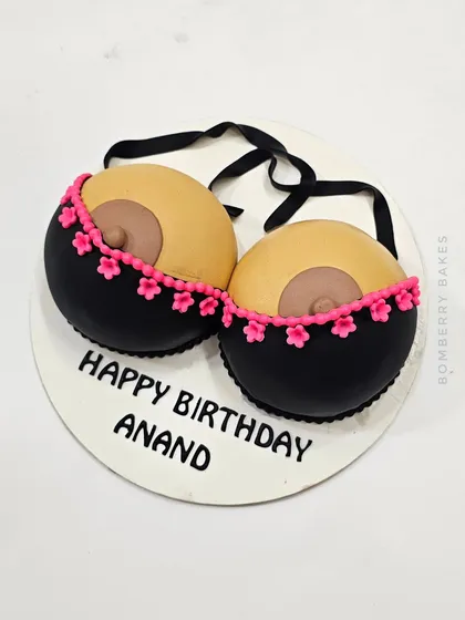 A "Happy Birthday Anand" cake with a playful, adult theme, featuring a sculpted bra.