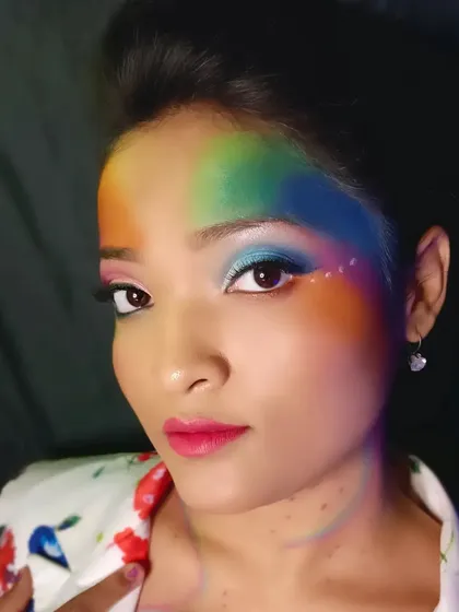 A direct look at the camera, showing the symmetry and blend of the rainbow colors on the face. The bright pink lip ties the whole look together.