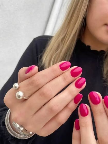 A beautiful, glossy magenta polish on perfectly shaped short nails, shown on a client.