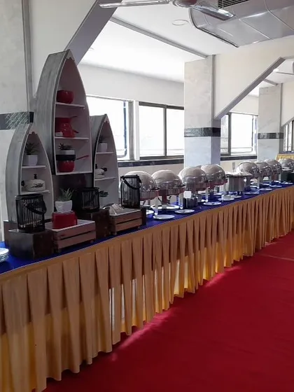 A full view of a buffet line inside a banquet hall with a red carpet. The boat shaped shelving units add a unique decorative element to the overall presentation.