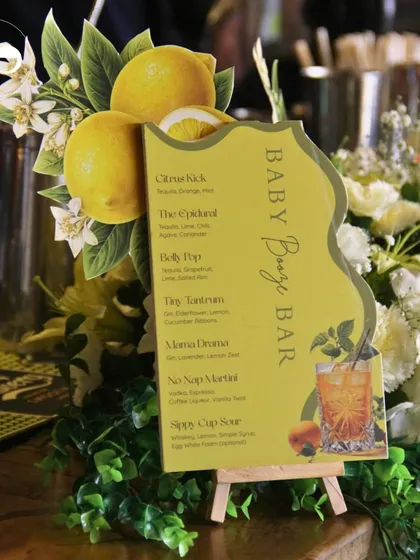 The 'Baby Booze Bar' menu nestled amongst fresh flowers and greenery, showcasing a cohesive and beautifully styled beverage station.