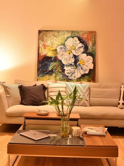 A neutral foundation in a living room acts as a versatile backdrop for seasonal updates and personalization. Here, a comfortable sofa is layered with pillows and a statement art piece to create a space that is both chic and cozy.