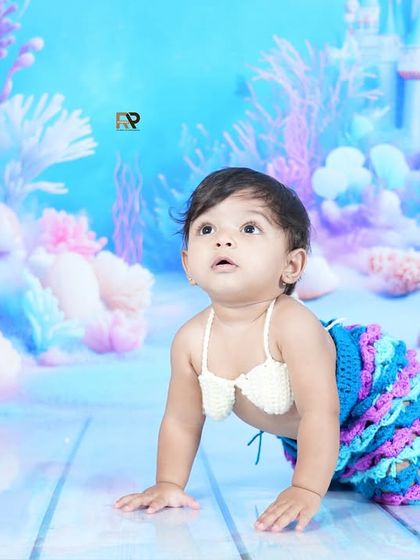 A baby mermaid looks up in wonder at a fish swimming by. This shot captures the magic and curiosity of our underwater-themed sessions.