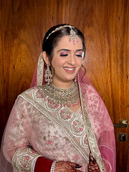 This bride's smile says it all. Her makeup features a beautiful pink eyeshadow that complements her pastel pink lehenga, creating a soft and cohesive bridal look.