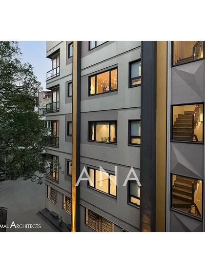 The side facade of the Yellow Line Apartment building at dusk. The windows reveal the internal staircase, and the vertical yellow element cleverly conceals plumbing shafts while becoming a key design feature.